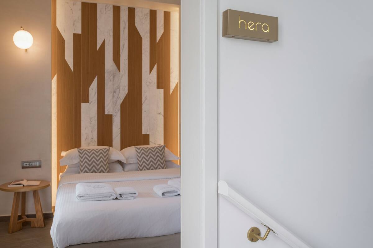 A hotel room with a bed, a round table, and a wall-mounted sign reading "hera".