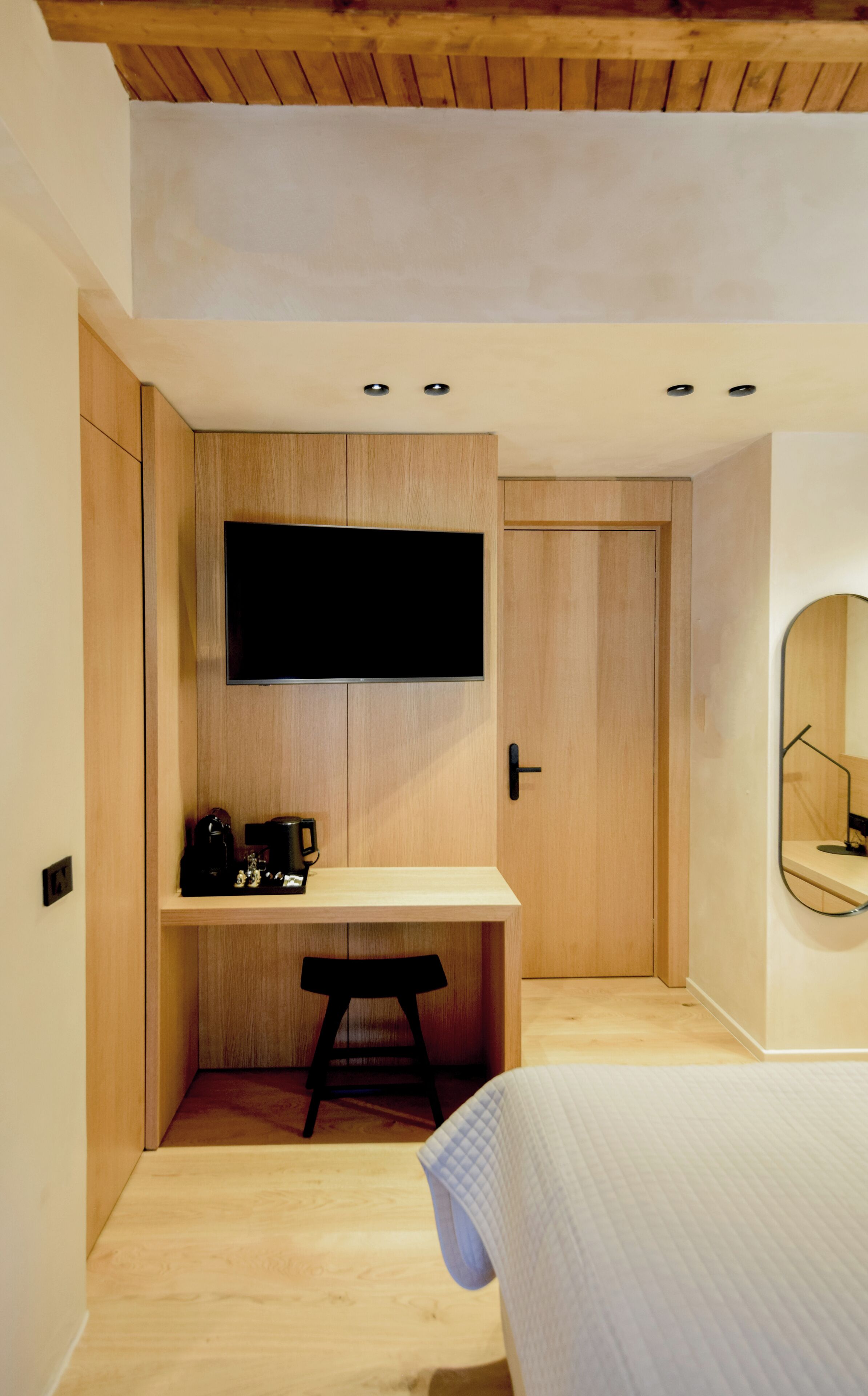 Un dormitorio moderno con un escritorio de madera, un televisor de pantalla plana, un taburete pequeño y una cama.