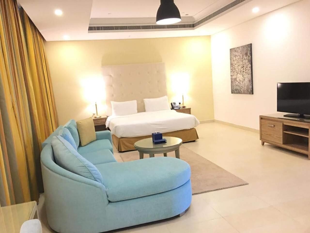 Une chambre d’hôtel moderne avec un grand lit, un canapé, une petite table ronde, un téléviseur et un tableau au mur.
