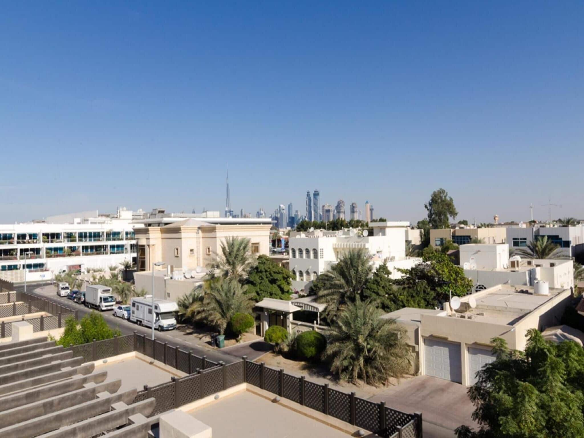 Un quartier résidentiel avec des bâtiments modernes, un ciel dégagé et une vue lointaine sur les contours d’une ville, notamment un grand gratte-ciel.