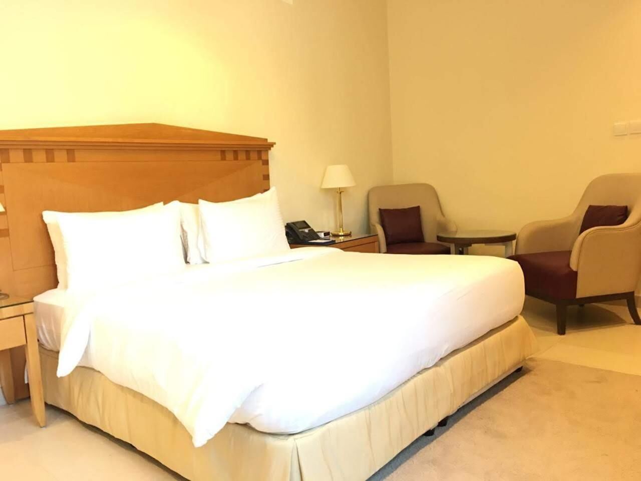 Une chambre d’hôtel avec un grand lit, une table de chevet, une lampe, deux fauteuils et une petite table.