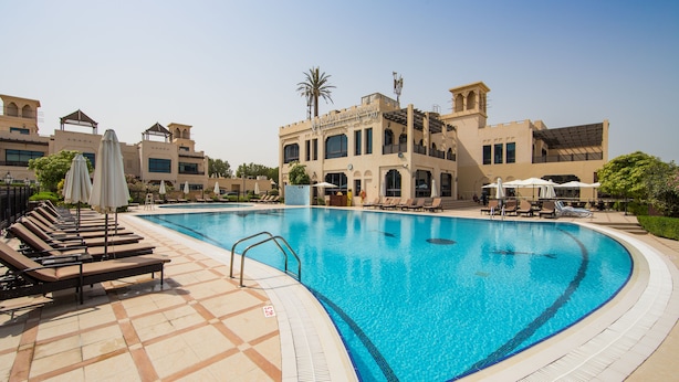 A swimming pool with lounge chairs and umbrellas, surrounded by a building with a tiled floor and a clear blue sky. - Roda Beach Resort (Dubai)
