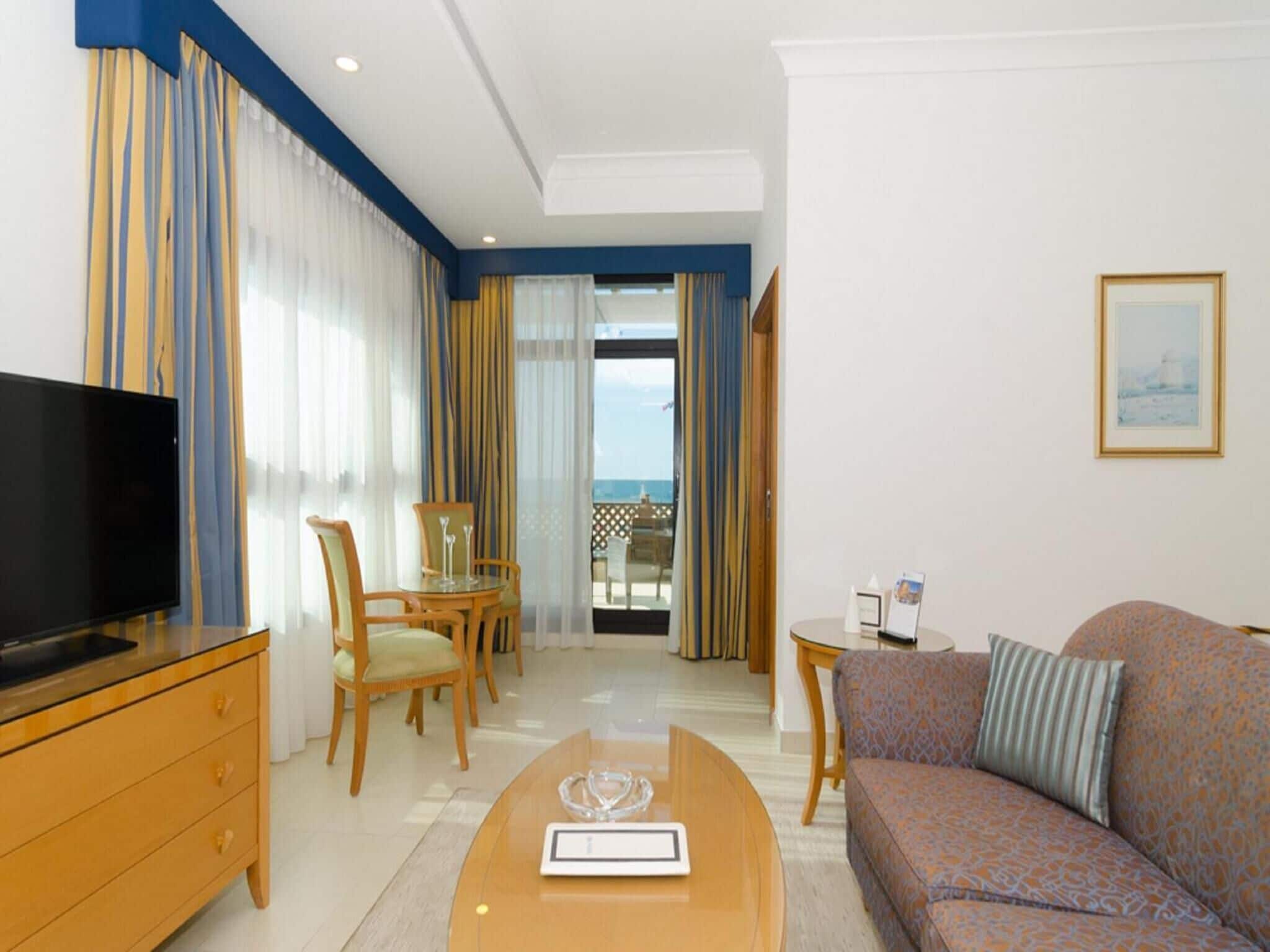 Een hotelkamer met een televisie, een bank, een eettafel met stoelen en een balkon met uitzicht.