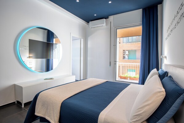 A modern bedroom with a large bed, a round mirror, a white dresser, and a balcony with a view. - Skyhouse Beverello (Naples)