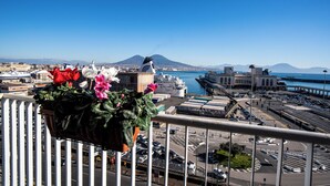 A balcony with a flower planter, a view of a busy port with ships and a mountain in the background. - Skyhouse Beverello (Naples)