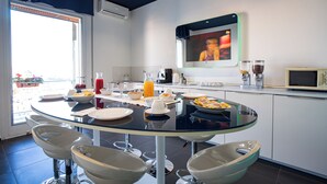 A modern kitchen with a glass dining table, white cabinets, and a large window. - Skyhouse Beverello (Naples)