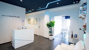 A modern reception area with a white desk, a potted plant, and a seating area with a white couch. - Skyhouse Beverello (Naples)