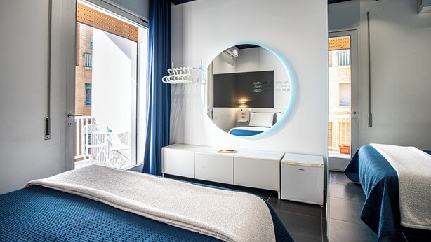 A modern hotel room with a large bed, a round mirror, a desk, and a view of the outside balcony. - Skyhouse Beverello (Naples)