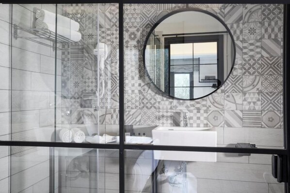 A bathroom with a glass partition, a round mirror, and patterned tiles.