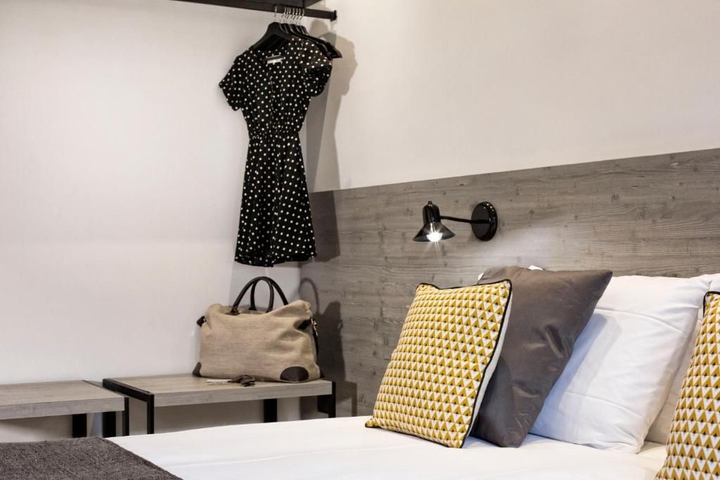 A hotel room with a bed, a nightstand, a hanging dress, a lamp, and a pillow.