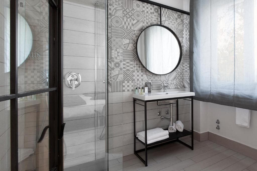 Une salle de bain moderne avec une douche à parois de verre, un miroir rond et un lavabo blanc doté d’un cadre noir.