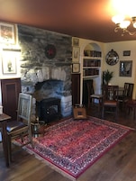Uma sala de estar acolhedora com lareira de pedra, móveis de madeira e um tapete vermelho estampado.