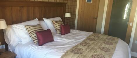 Un dormitorio con una cama grande, cabecera de madera, mesita de noche con una lámpara y una puerta con un letrero.