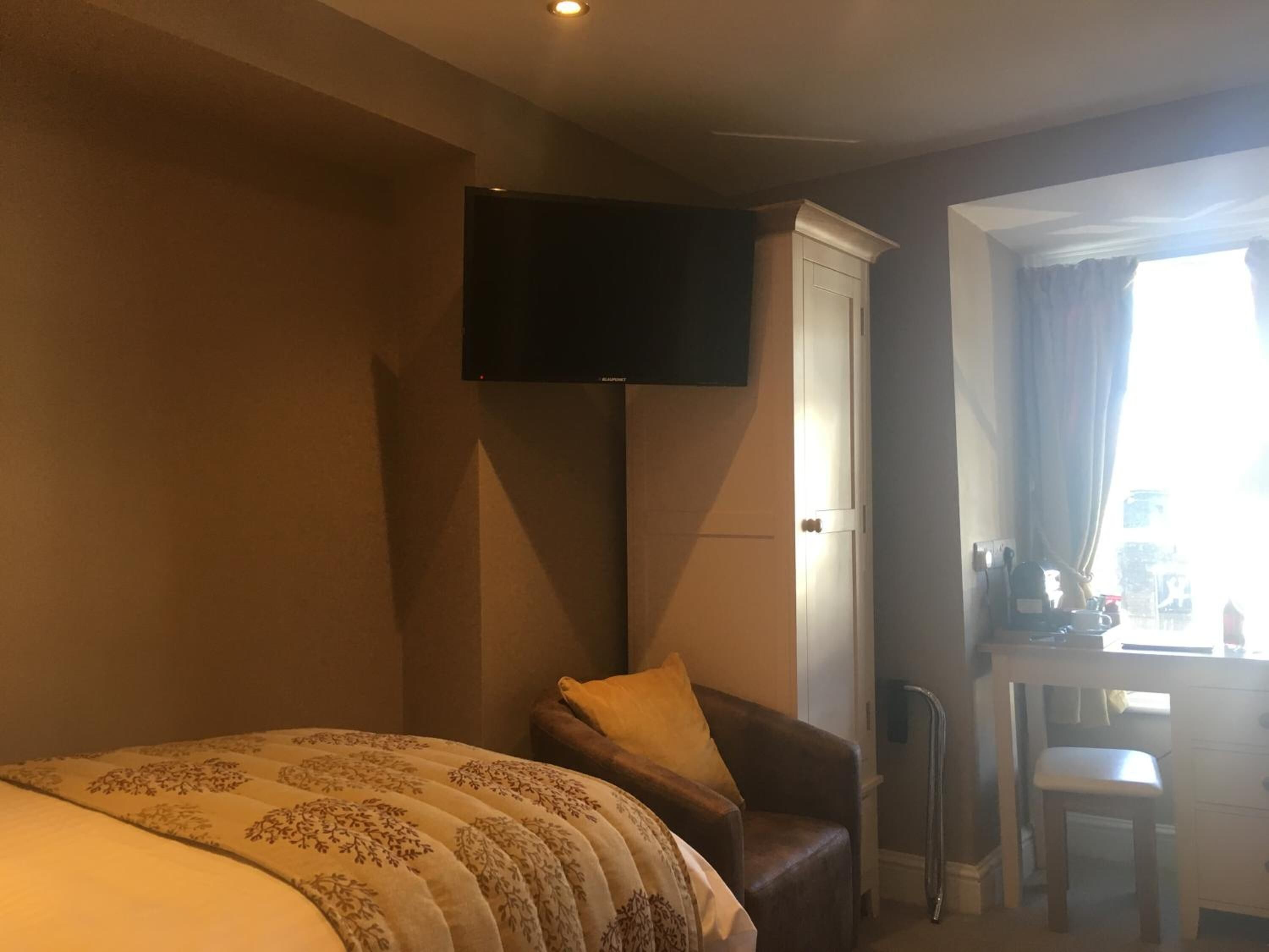 A hotel room with a bed, a chair, a desk, a television, and a window with curtains.
