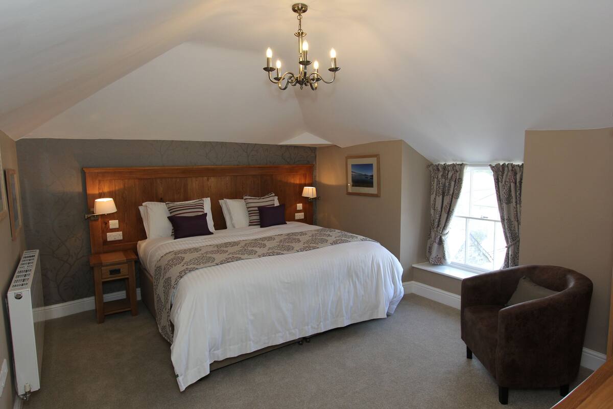 A bedroom with a large bed, a wooden headboard, a chair, a radiator, and a window with curtains.