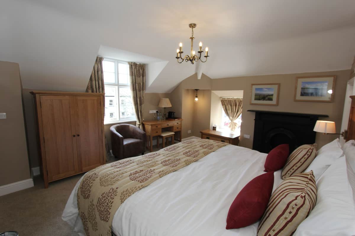 A bedroom with a large bed, a desk, a chair, a wardrobe, a fireplace, and a chandelier.