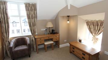 A room with a desk, chair, and a small cabinet. There is a window with curtains, a lamp, and a light fixture.
