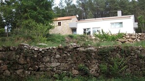 A stone wall in front of a modern house with a tiled roof, surrounded by greenery and trees. - Quinta dos Caibrais (Oliveira de Frades)