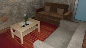 Un salon avec un mur en pierre, un canapé beige, une table basse en bois et un tapis à rayures rouges.