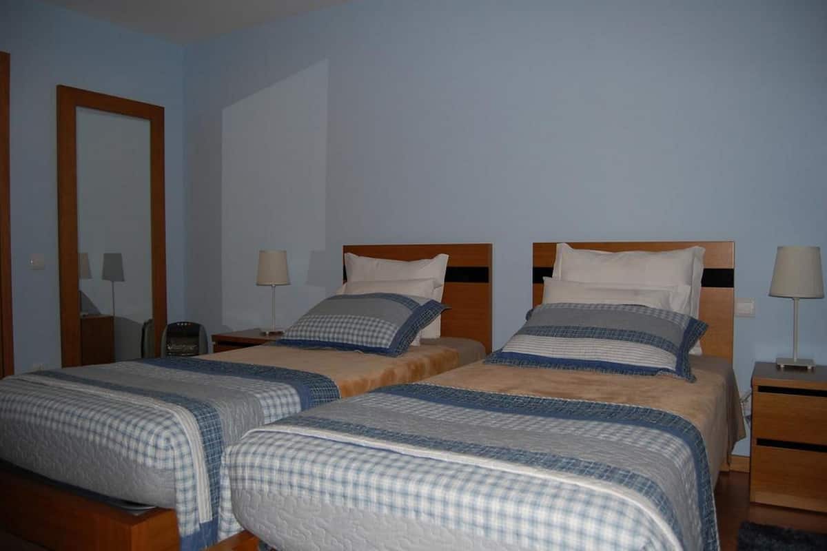 Ein Hotelzimmer mit zwei Einzelbetten, Holz-Kopfteilen, Nachttischen mit Lampen und einem großen Spiegel an der linken Wand.