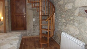 A room with a spiral staircase, stone walls, a wooden door, and a radiator. - Quinta dos Caibrais (Oliveira de Frades)