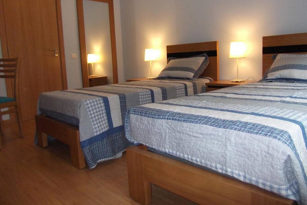Ein Hotelzimmer mit zwei Betten, Holzkopfteilen, Nachttischlampen und einem Holzstuhl.