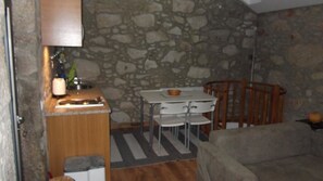 Une petite pièce aux murs de pierre, équipée d’un coin cuisine, d’une table à manger avec des chaises et d’une chaise en bois.