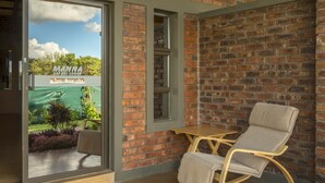 A room with a brick wall, a glass door leading outside, a wooden rocking chair, and a small table.