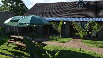 A patio area with picnic tables and umbrellas, a brick pathway, and a building with a tiled roof.