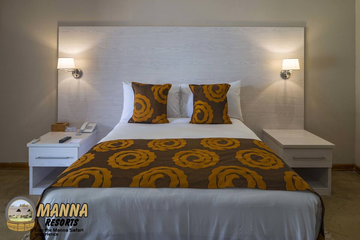 A hotel room with a large bed, two bedside tables, a nightstand, a lamp, and a phone.