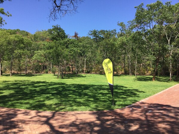 A grassy area with a yellow sign, trees, and a brick path.