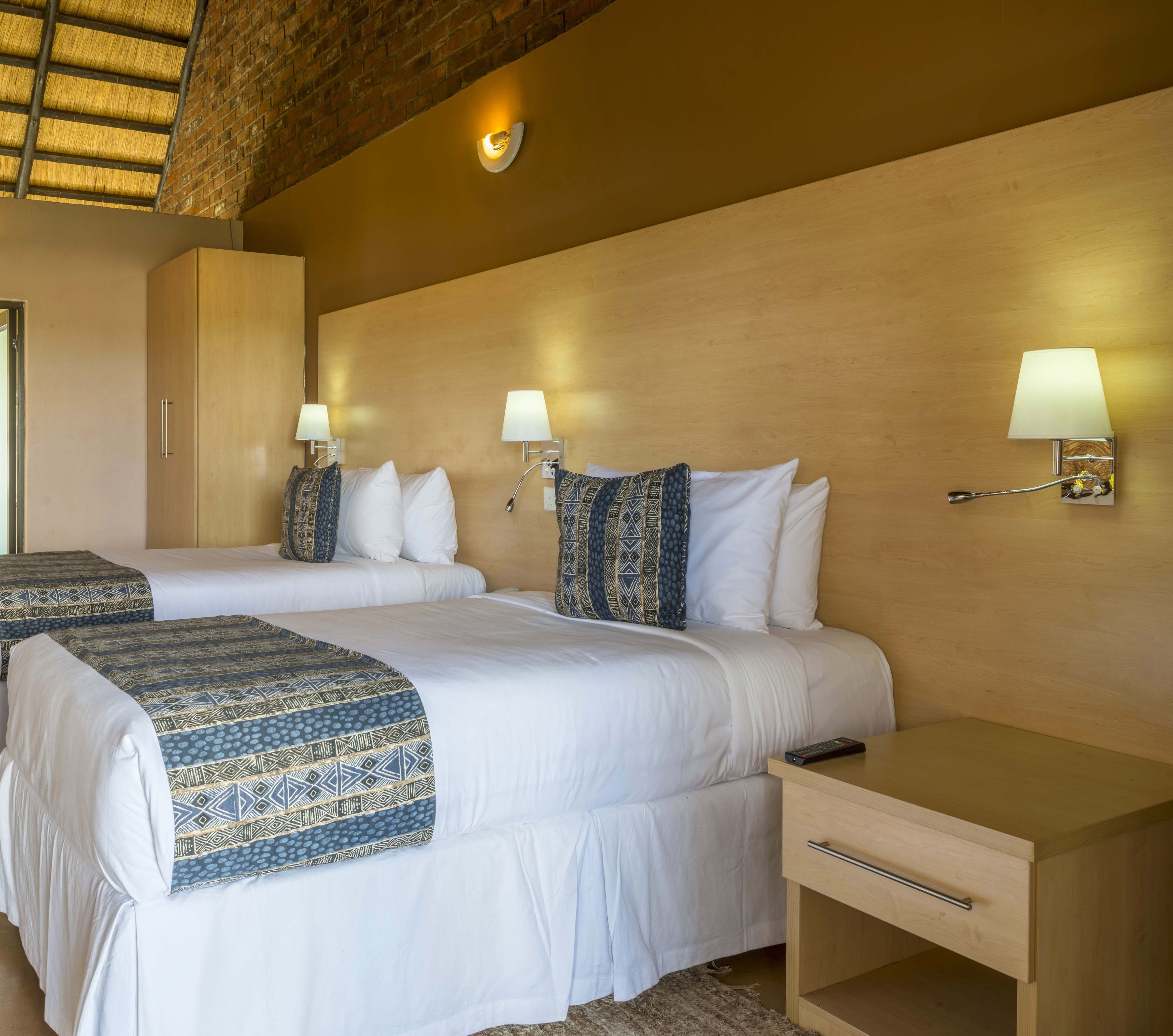 Habitación de hotel con dos camas, un armario de madera, una mesita de noche y lámparas fijadas a la pared.