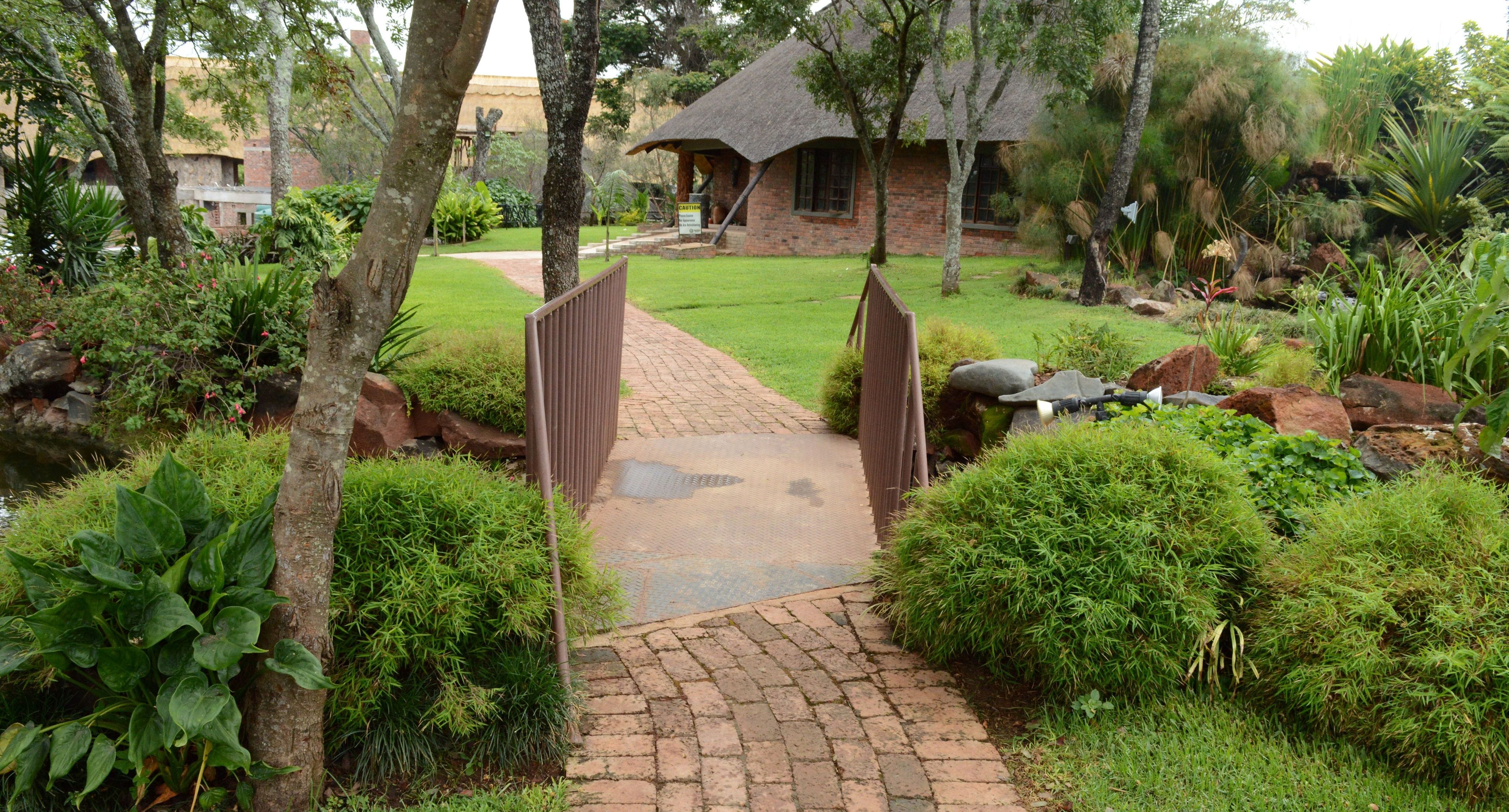 A pathway leading to a thatched-roof building surrounded by lush greenery and rocks.