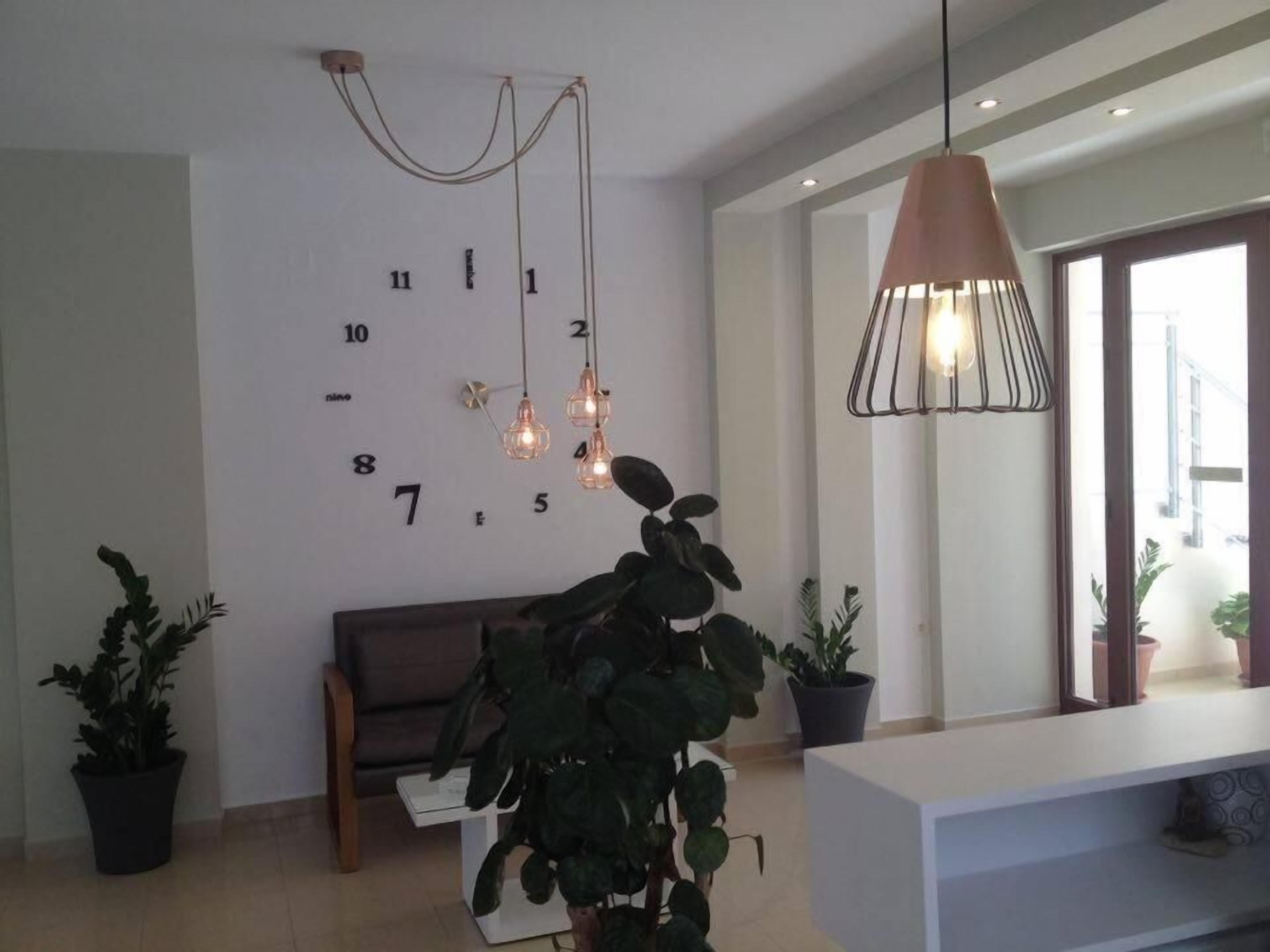A modern living room with a large wall clock, a sofa, a coffee table, and potted plants.