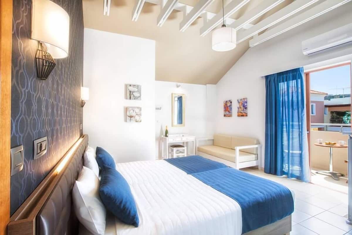 A hotel room with a bed, a small desk, a chair, a window with curtains, and a balcony.