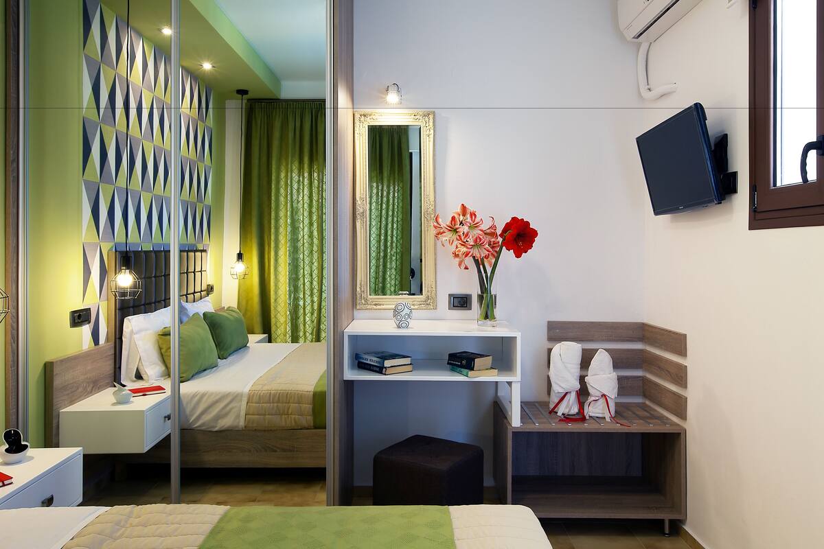 A modern hotel room with a bed, bedside table, mirror, and a small desk with a chair.