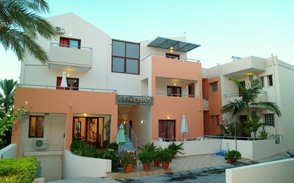 A multi-story hotel with balconies, a covered entrance, and potted plants.