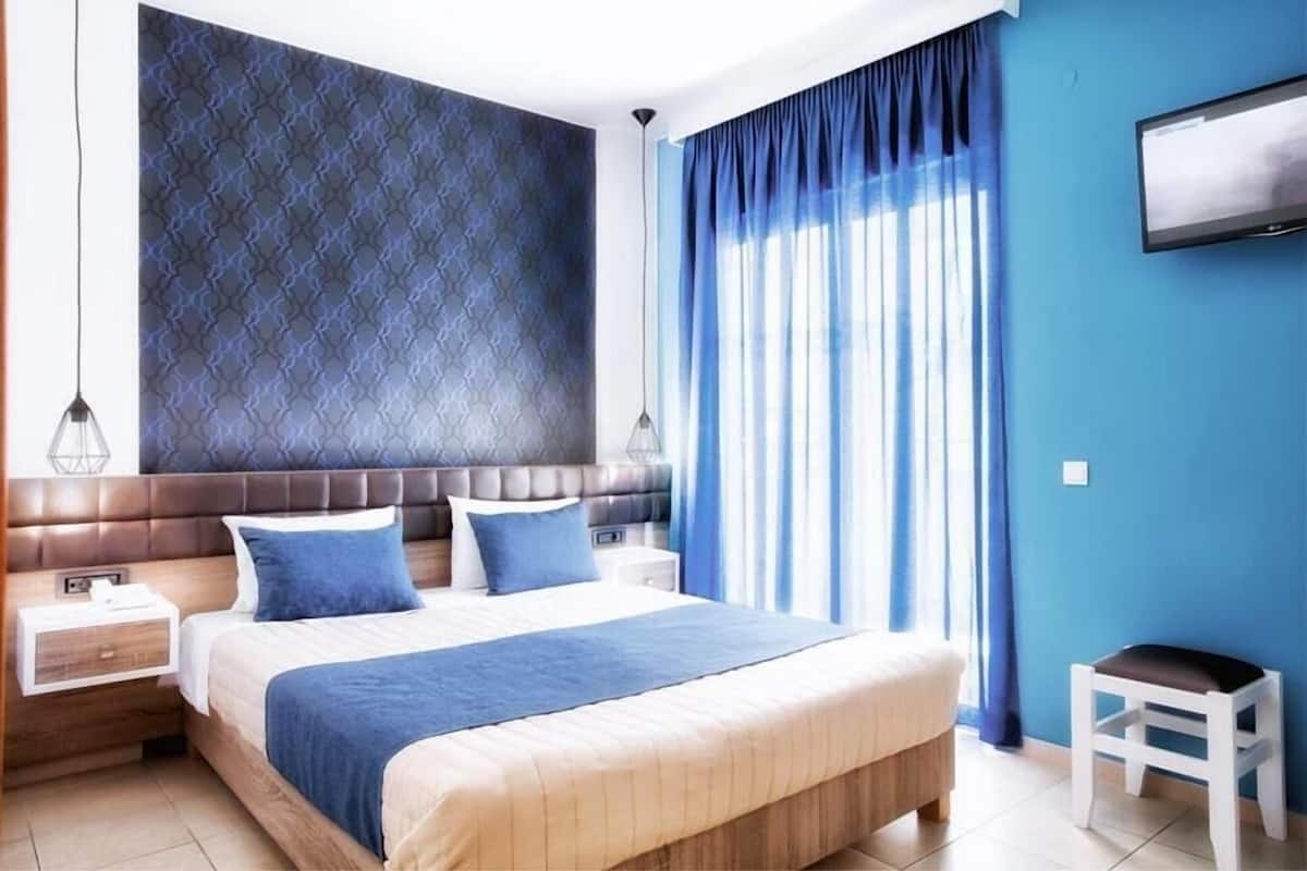 A modern bedroom with a large bed, a headboard, a nightstand, a TV, and a window with curtains.