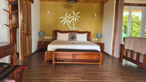 Una cama con estructura de madera y cabecera, dos mesitas de noche con lámparas, un perchero de madera y vistas a zonas verdes.