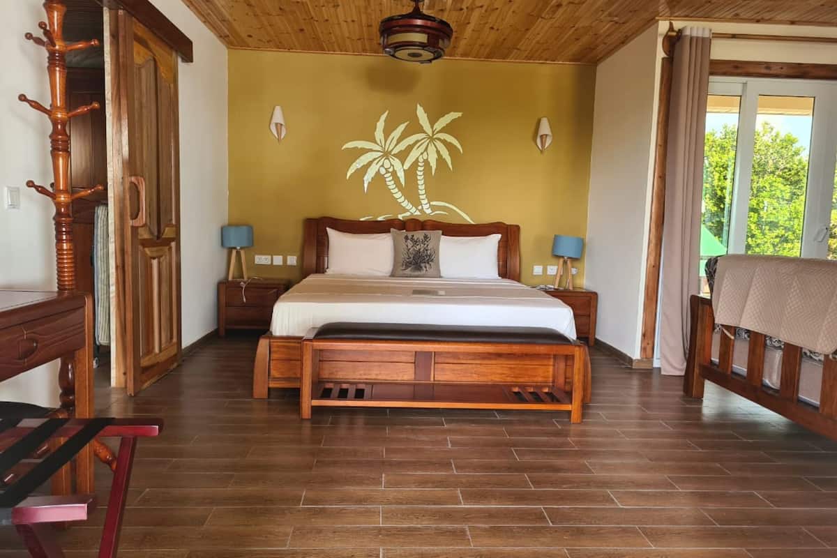 Una cama con estructura de madera y cabecera, dos mesitas de noche con lámparas, un perchero de madera y vistas a zonas verdes.