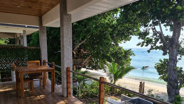 Una terraza de madera con una mesa y sillas que da a una playa con un bote en el agua.