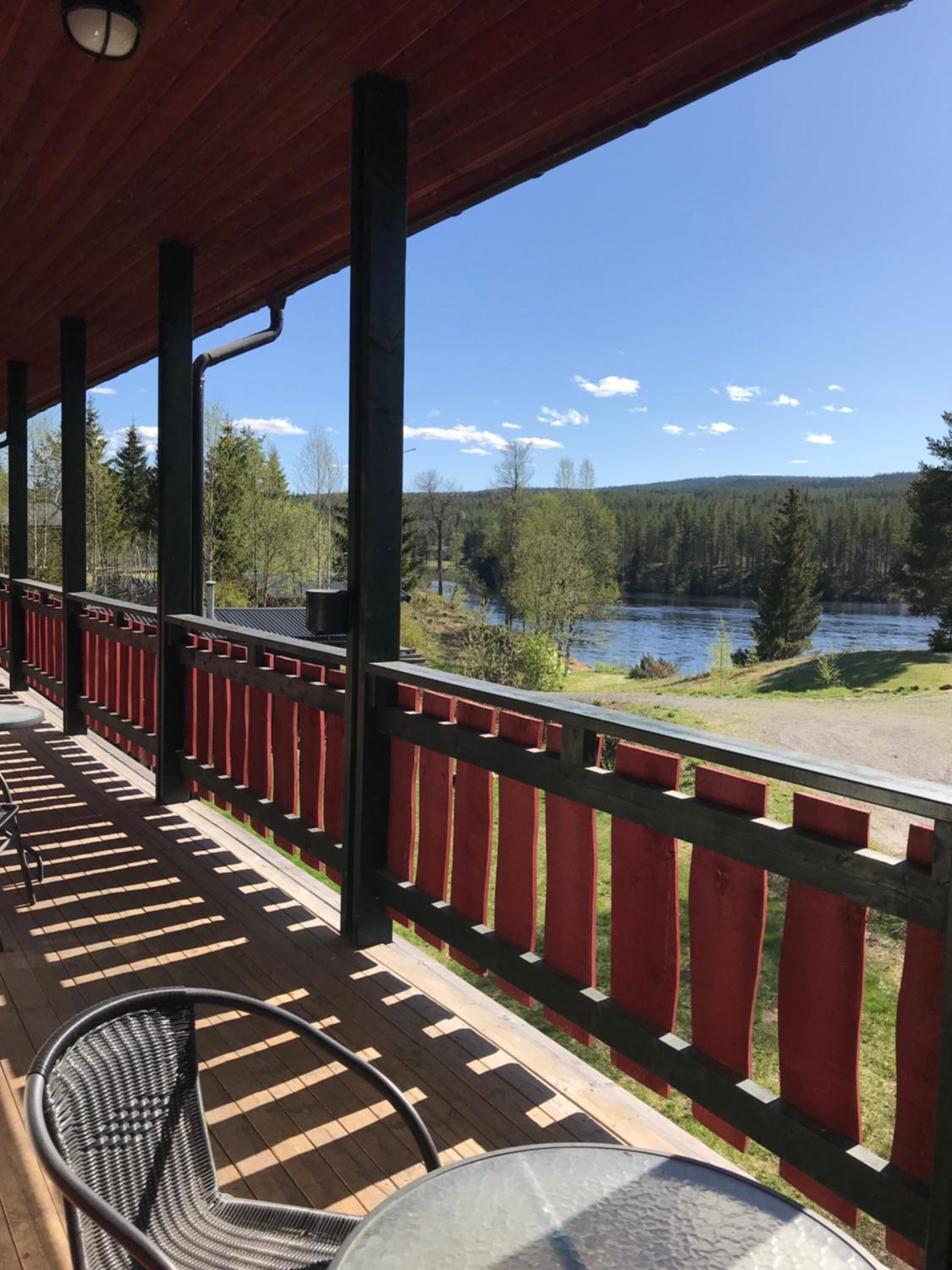 A covered outdoor area with a wooden deck, red railings, and a view of a lake and forest.