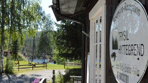 A reception sign for a hotel named Trisil in Hettegrand, with a view of a lake and a wooden fence in the background.