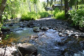 A stream with rocks and greenery, a wooden cabin, and a forested area. - Trysil Motel & Vandrerhjem - Hostel (Trysil)