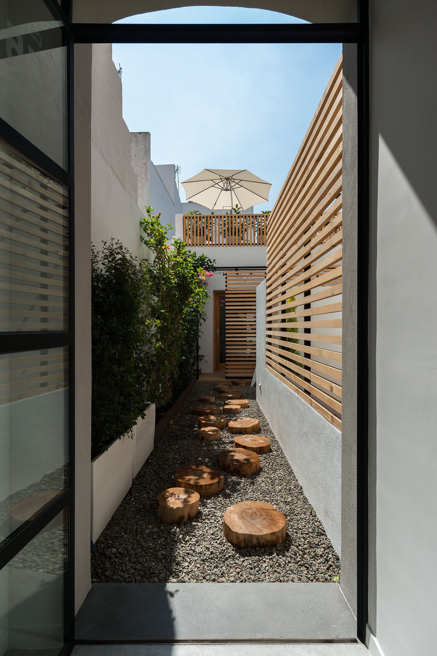A narrow pathway with wooden slats, a wooden fence, and a small garden area with stepping stones and plants.