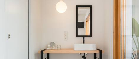 Une salle de bain moderne avec un lavabo blanc, un miroir et un luminaire suspendu.