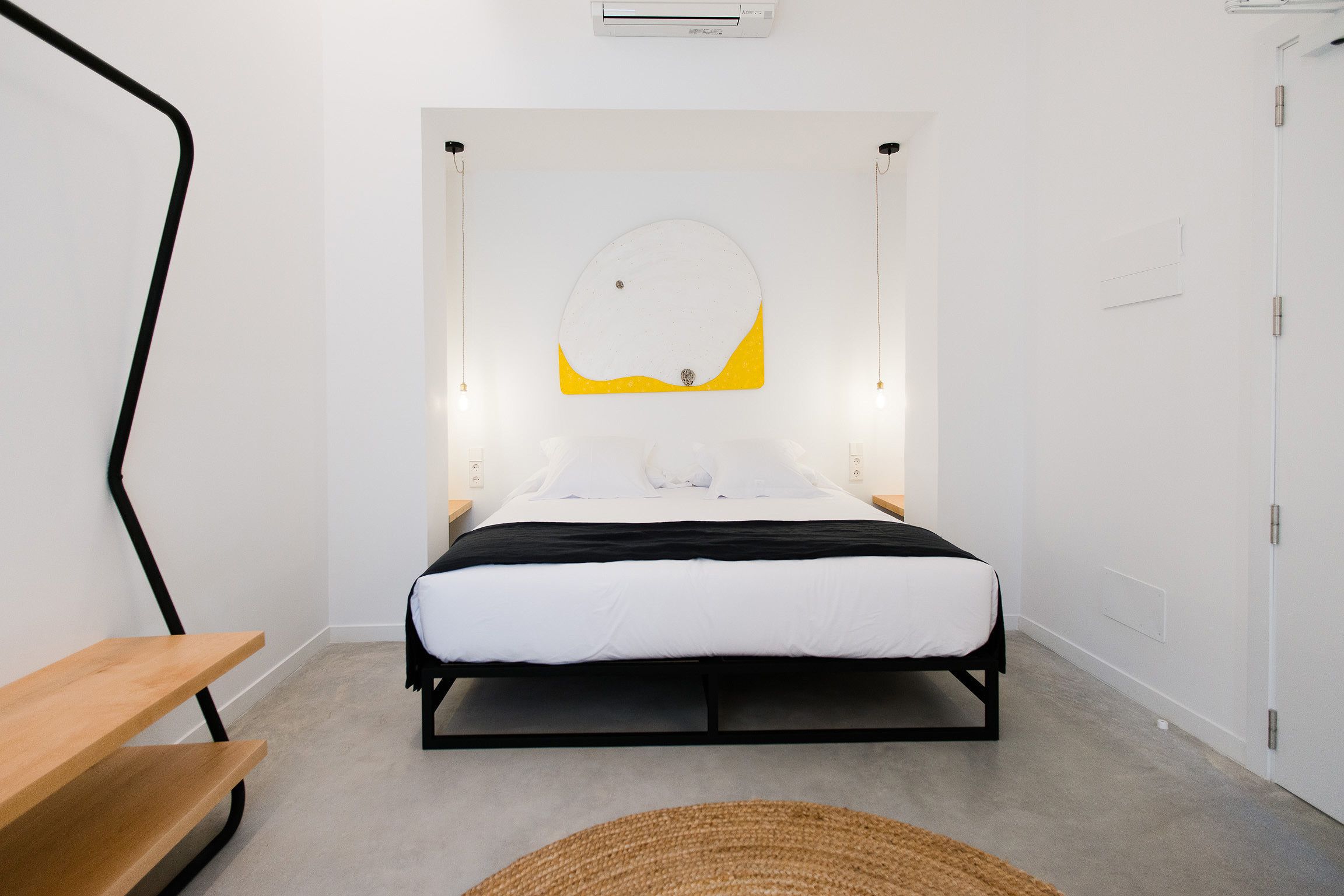 A modern bedroom with a bed, a wooden bench, and a circular light fixture above the bed.