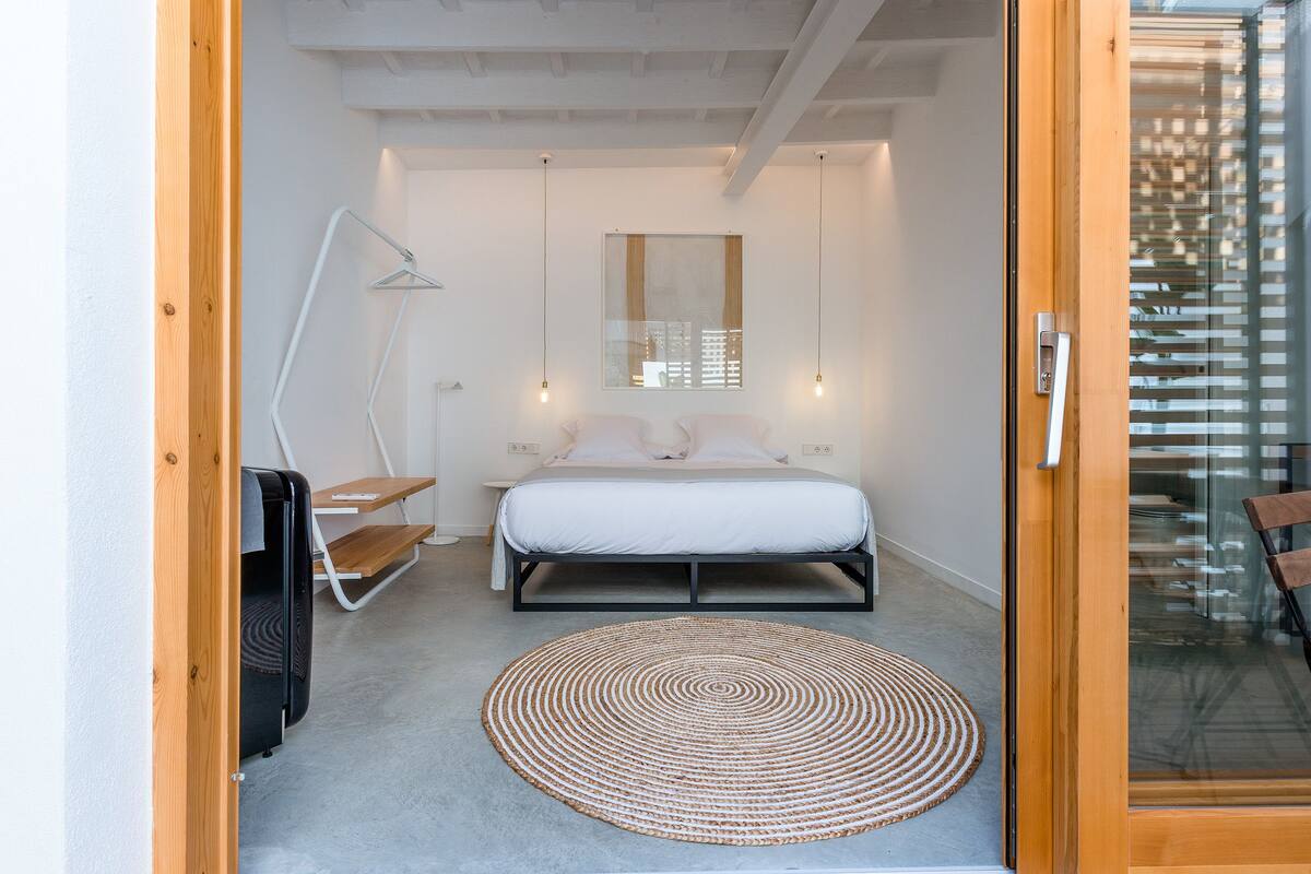 A modern bedroom with a bed, bedside tables, a hanging lamp, and a large window.