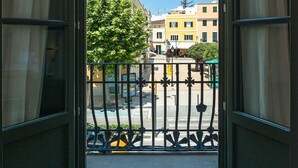 Uitzicht vanaf een balkon met een metalen hekwerk, op een straat met gebouwen en een boom.