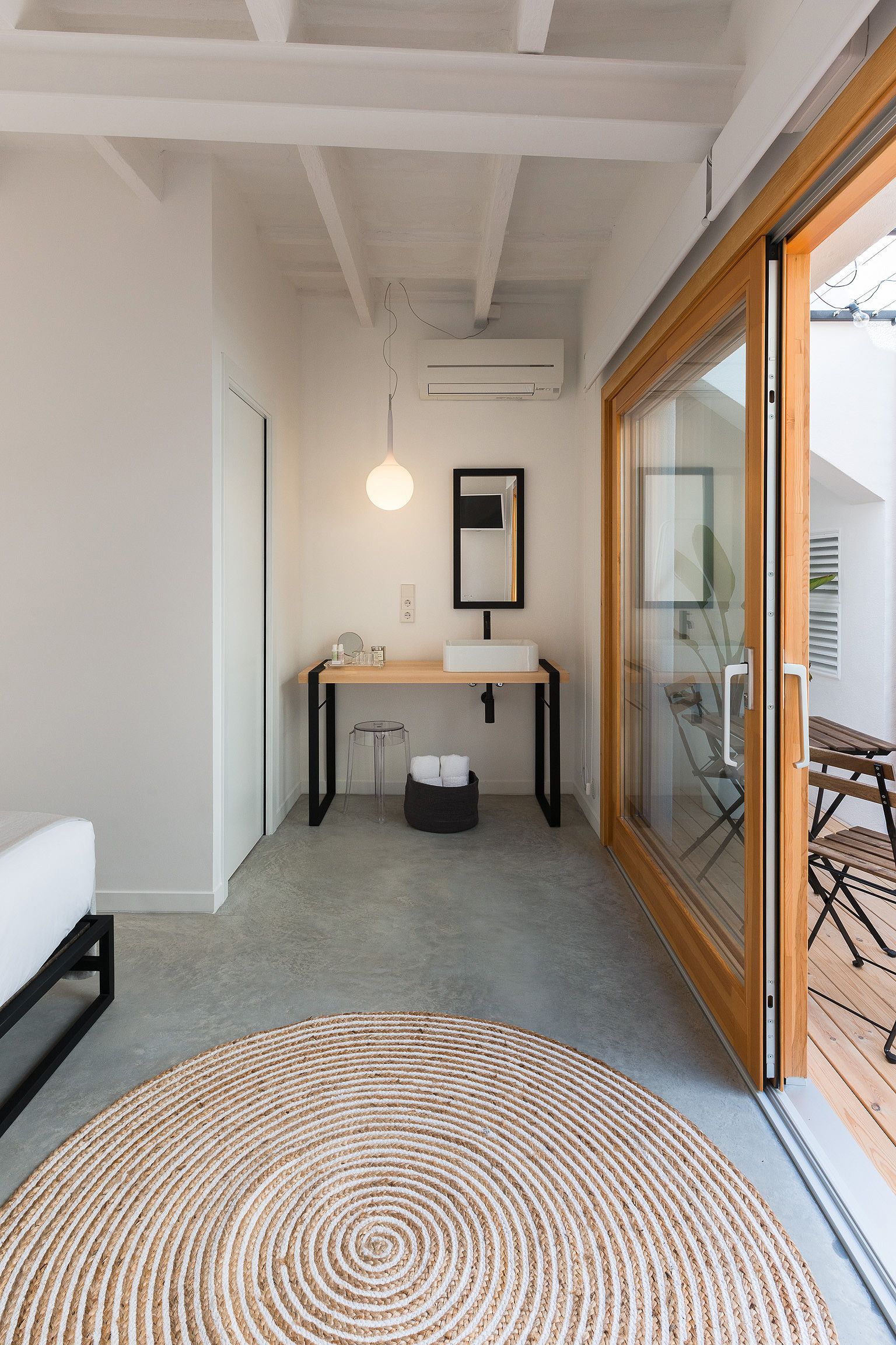 A modern bathroom with a wooden vanity, a round rug, and a glass door leading to an outdoor area.